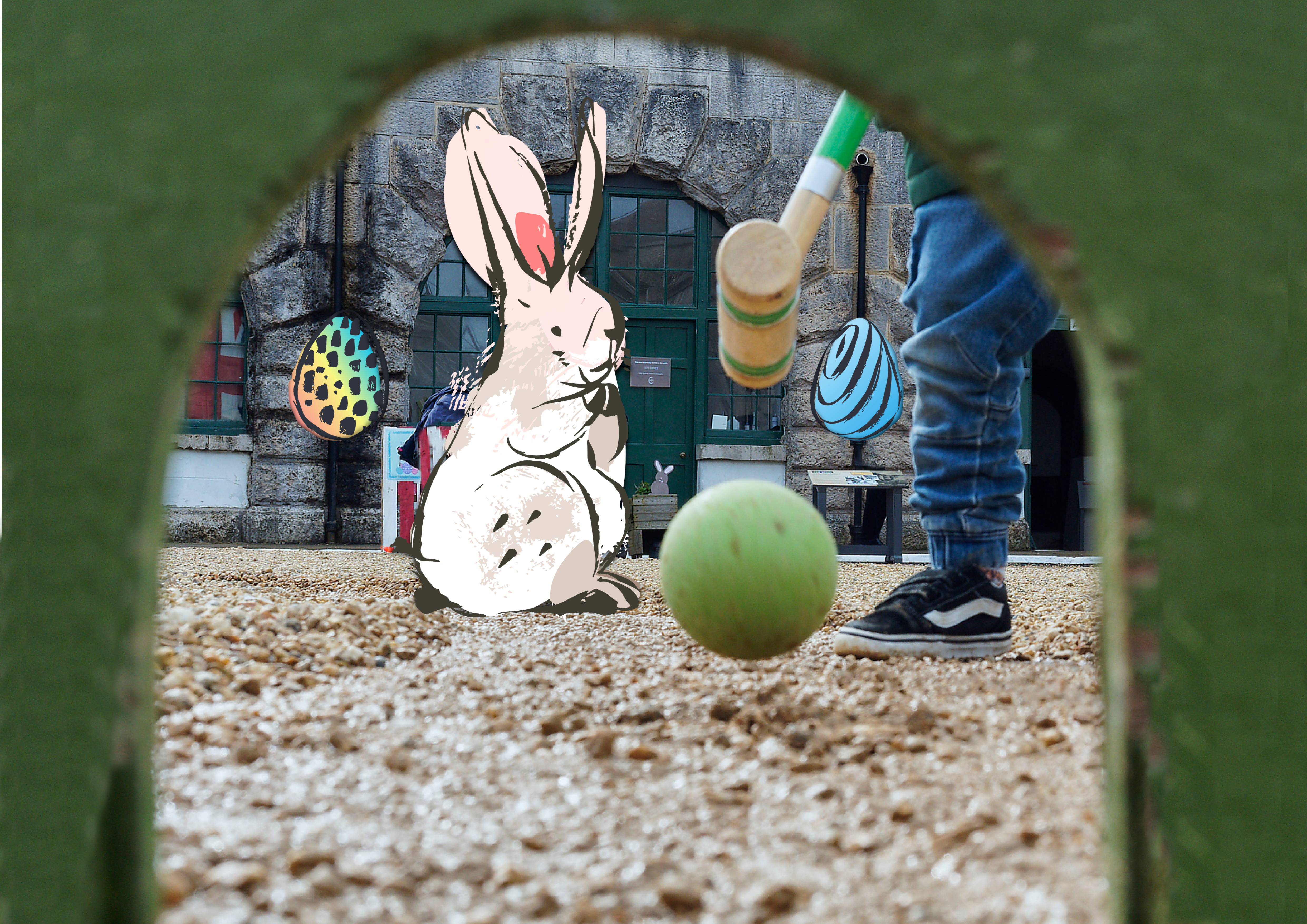 A white cartoon rabbit watches a child play. They are both situated in Nothe Fort. On the stone wall behind are multicoloured Easter Egg decorations. The child is only partially in frame, and is hitting a green ball with croquet mallet into a green tunnel. The tunnel arch frames the image.