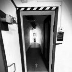 A black and white image of a thick metal door to an emergency nuclear bunker. The corridor beyond the door is dark, but there is a mysterious light at the end of the tunnel. The Text reads COLD WAR BUNKER TOURS