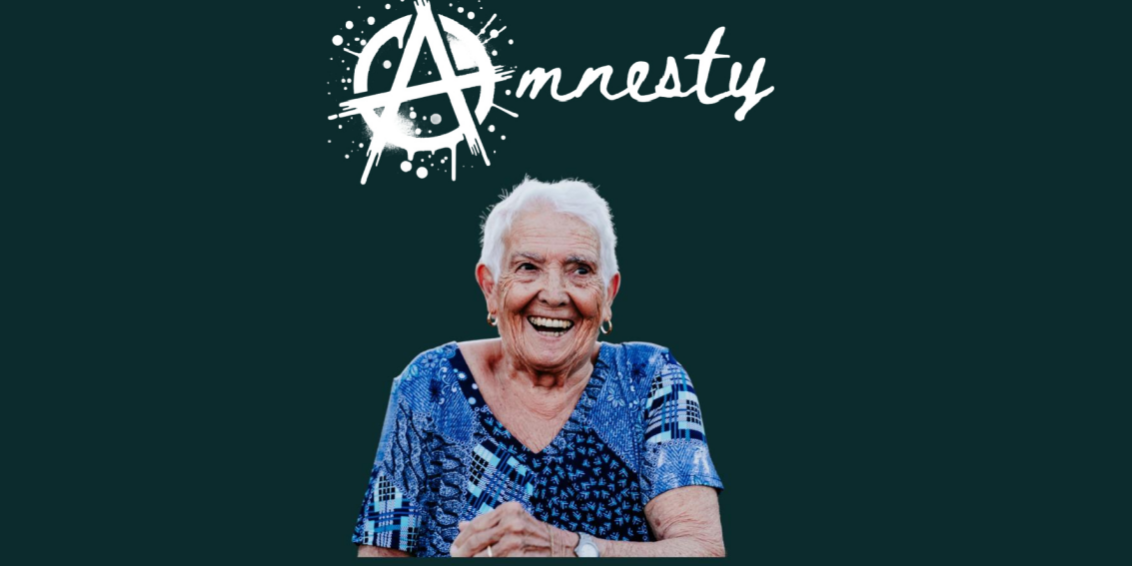 A tile sized image with a WHITE font that reads 'AMNESTY' with the A resembling the Anarchy symbol. There is a photo in the centre of an older woman in a blue top smiling with a cheeky grin. The text beneath reads: Did you break into Nothe Fort between 1956 and 1979? Tell us your story!
