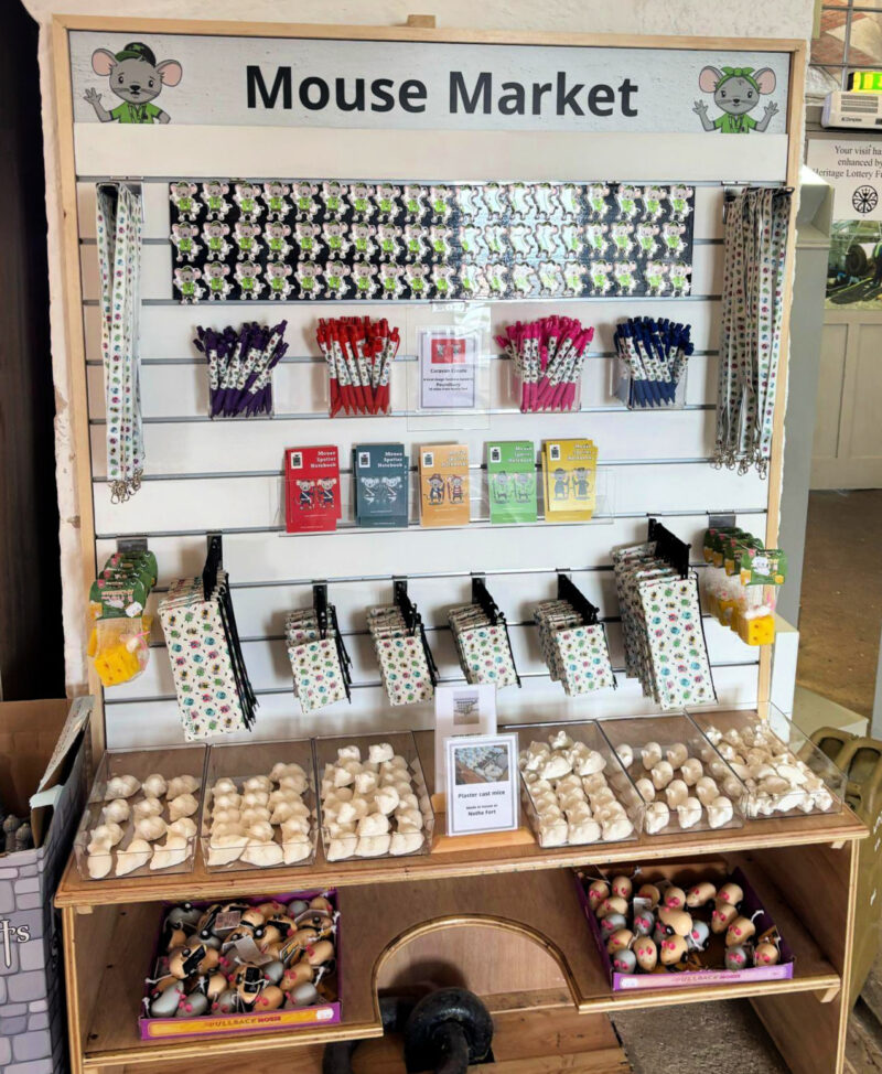 A photo of the Mouse market shelves in the Fort gift shop, featuring white mice from our famous Mouse Hunt, key rings, magnets, and note books with the characters Warren and Winnie Mice.