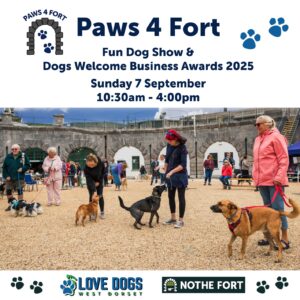 People walking and socializing with dogs on leads at a previous dog show with historic stone arches of the Fort in the background; event banners and logos are visible.