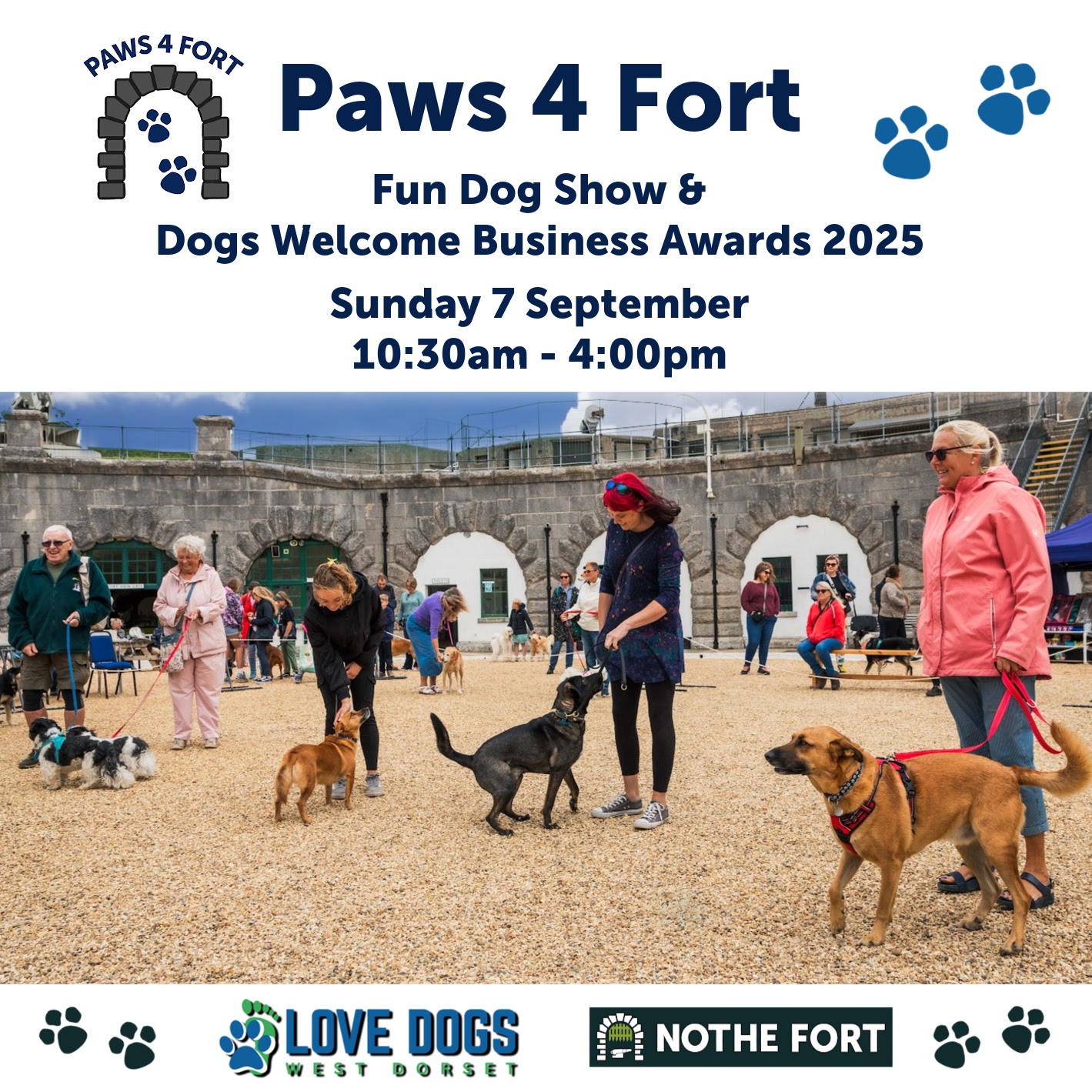 People walking and socializing with dogs on leads at a previous dog show with historic stone arches of the Fort in the background; event banners and logos are visible.