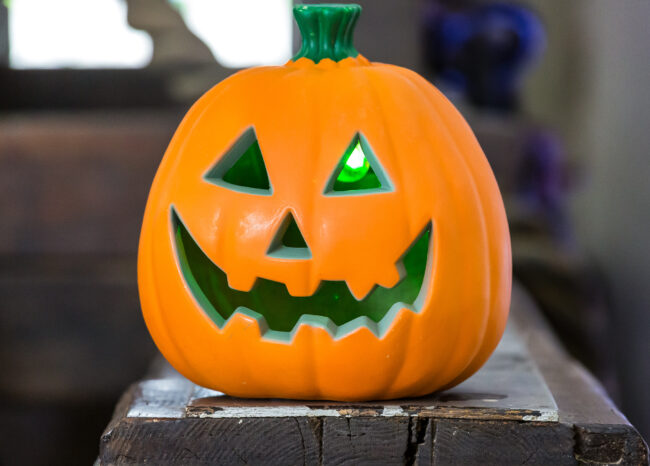 A smiley spooky carved pumpkin sits on a wooden beam in the Fort.