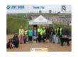 A line up of 12 human volunteers and staff, and three fine dogs represent the Love Dogs West Dorset and Nothe Fort teams. Behind them is a Nothe Fort white and green gazebo, and the walls of the Fort. Above them in blue text reads a thank you message.