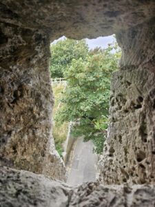 The view from the defensive slits in the Barbican wall show the approach to the Fort, with green trees and a road below. 