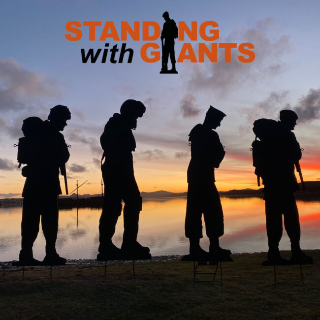 Four metal soldier silhouettes stand against an orange and blue sunset background. The black and orange logo for Standing With Giants is imposed above them on a pale lilac sky.