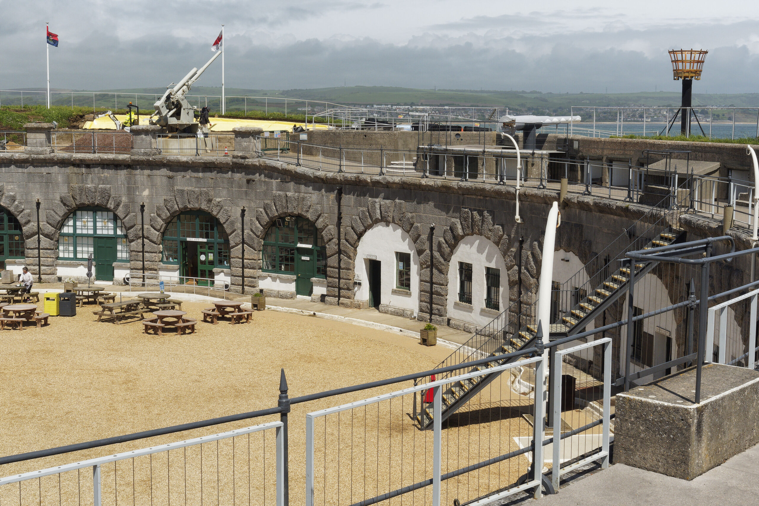 A very similar view of the Fort casemates and ramparts taken in 2024 to contrast with the older images of the Derelict Fort in the 1970s. The parade ground and ramparts are tidy, clear of rubbish, grass is cut and the three flagpoles are adorned in flags blowing in the wind against a blue sky.