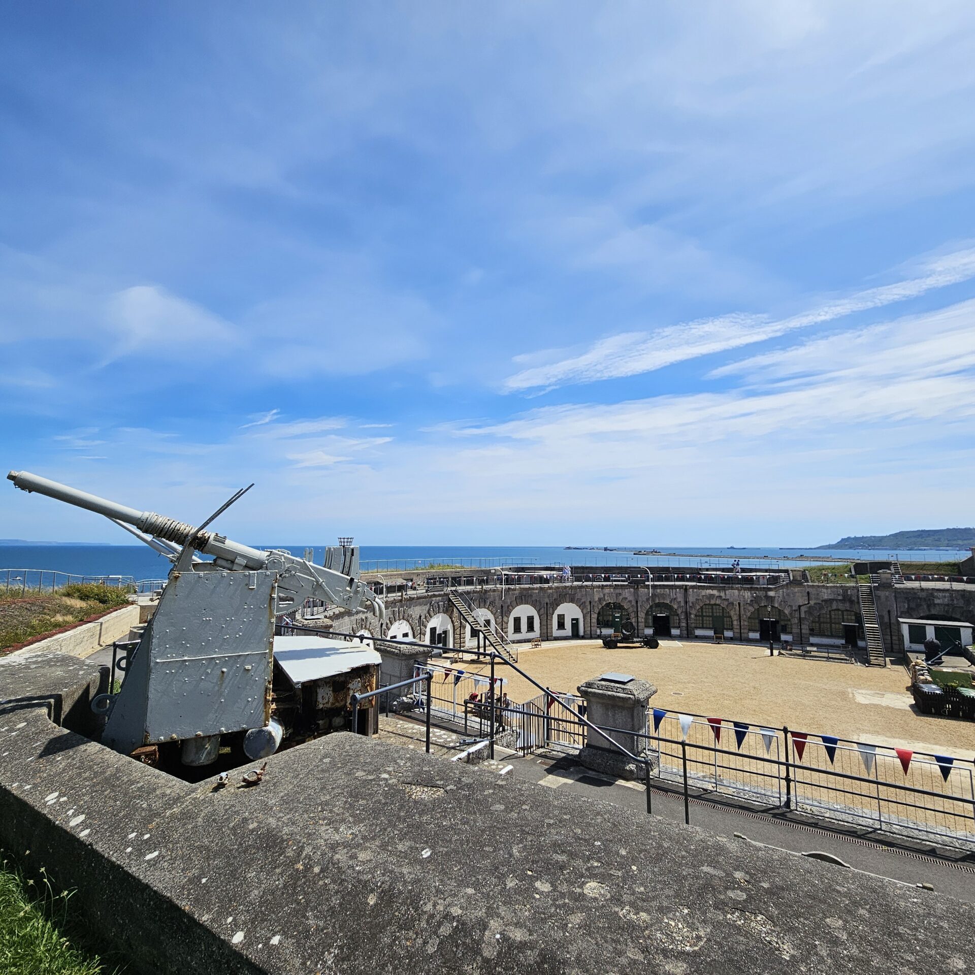 A panoramic view of the Fort taken from the ramparts. In the photo are the anti air craft guns, and you can see the curved walls of the Fort. In the distance is the sea and the Isle of Portland.