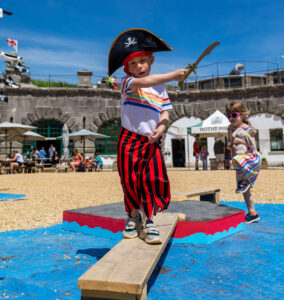 A young child on in pirate gear is walking the plank on the Fort pirate ship.