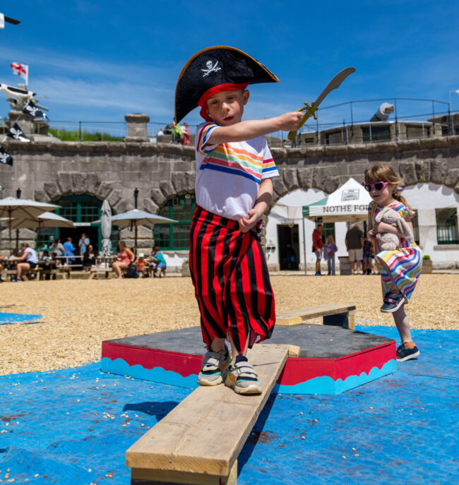 A young child on in pirate gear is walking the plank on the Fort pirate ship.