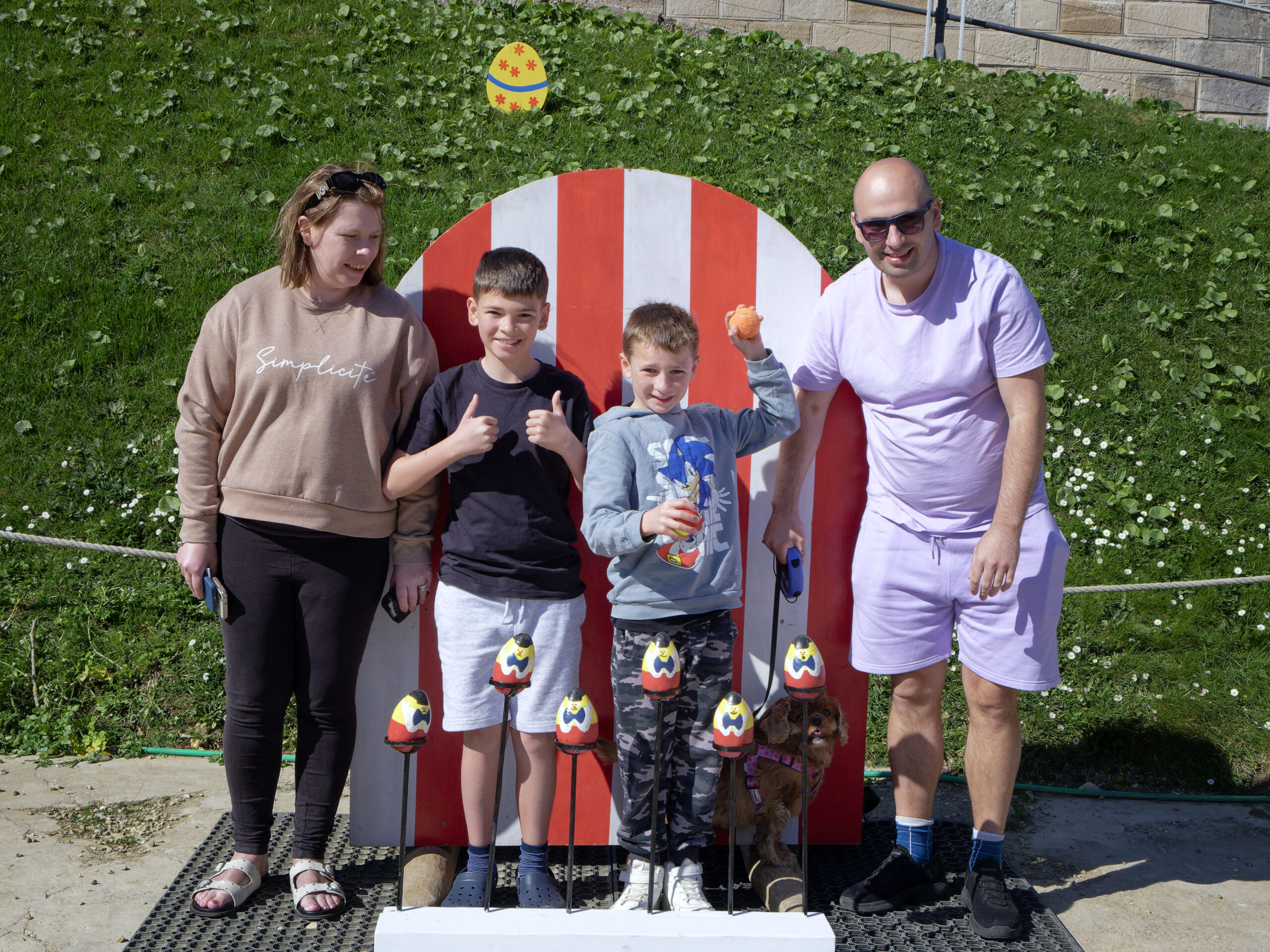 family of four stand in the parade ground in front of an Easter themed coconut shy throwing game.