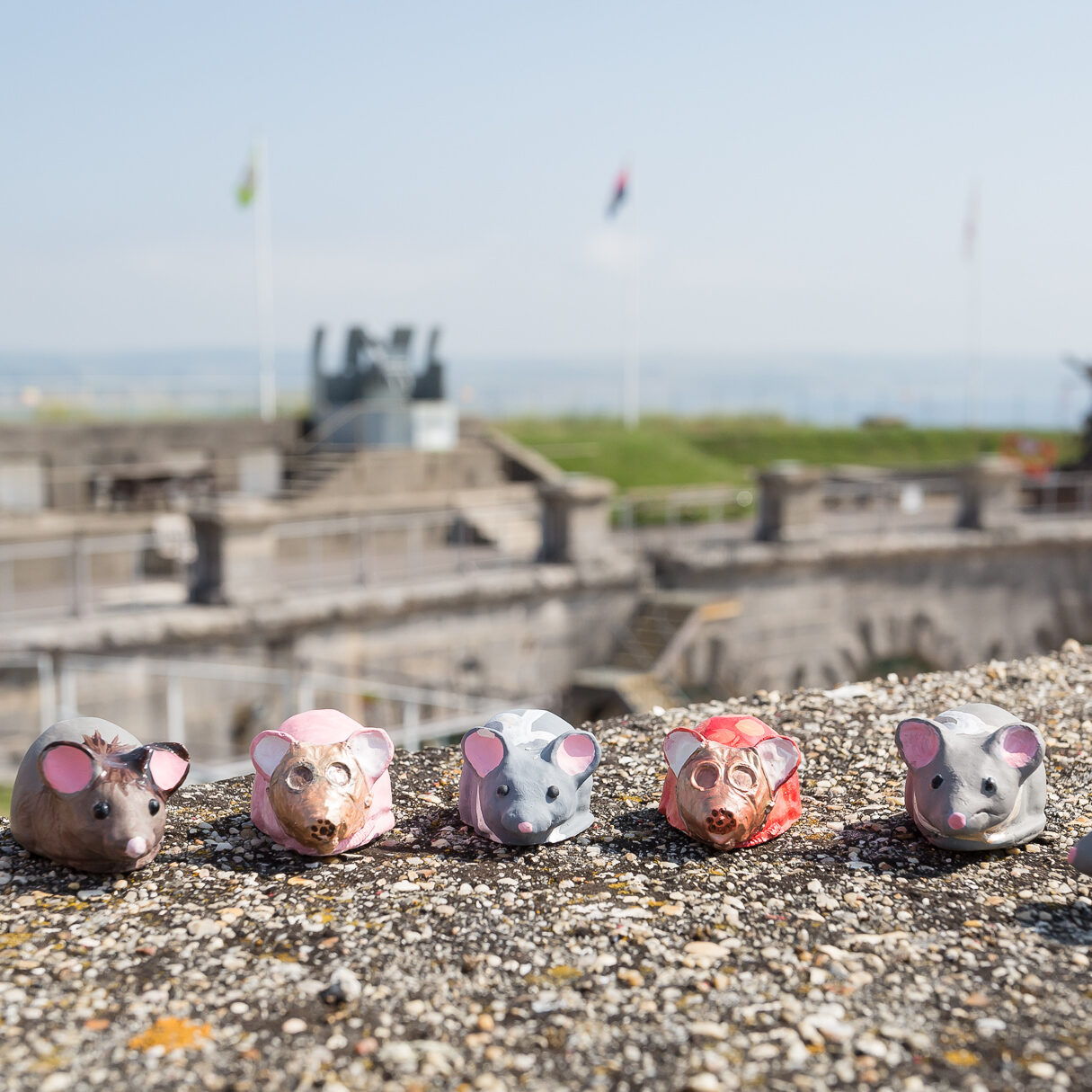 A photo of several painted clay mice sitting on the walls of the Fort. The anti-aircraft guns are blurred in the background.