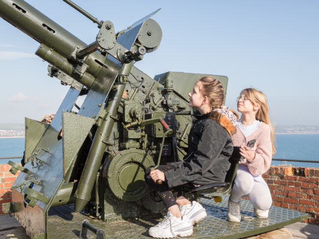 LG5A7421 Two young girls sit in the chair of the large green BOFUS gun that sits high on the ramparts.