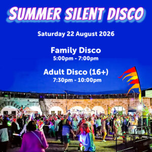A photo of a previous silent disco at dusk in the parade ground of Nothe Fort. The stone walls are lit up with orange lights and in the centre of the image, a crowd of people are dancing and partying, waving glow sticks and wearing glowing headphones. At the top of the image, across a deep blue night sky, there is a glowy holographic looking font that reads "SUMMER SILENT DISCO Saturday 22 August"