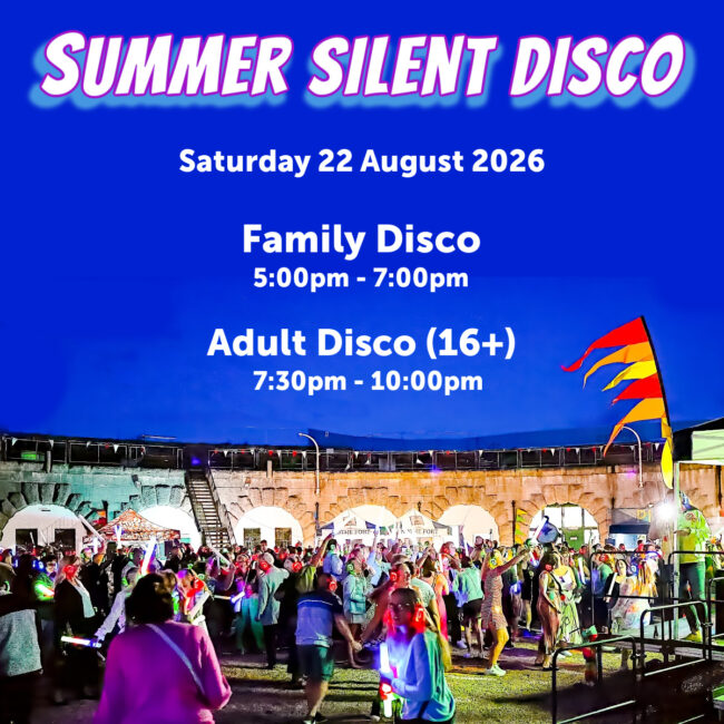 A photo of a previous silent disco at dusk in the parade ground of Nothe Fort. The stone walls are lit up with orange lights and in the centre of the image, a crowd of people are dancing and partying, waving glow sticks and wearing glowing headphones. At the top of the image, across a deep blue night sky, there is a glowy holographic looking font that reads "SUMMER SILENT DISCO Saturday 22 August"