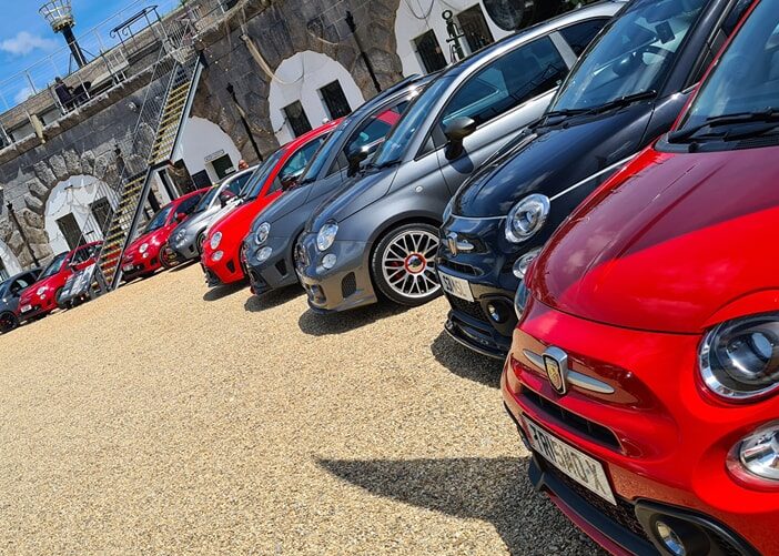 A tilted angle photo of a ring of different coloured cars parked in the parade ground.