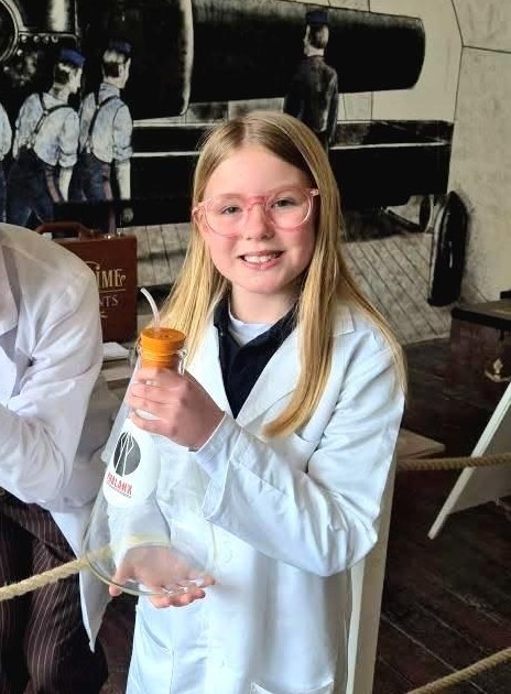 A young girl in a lab coat is holding a glass beaker, prepared to do scientific experiments.