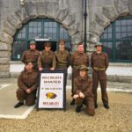 The WW2 Garrison pose in the Parade Ground in front of a wartime recruitment poster.