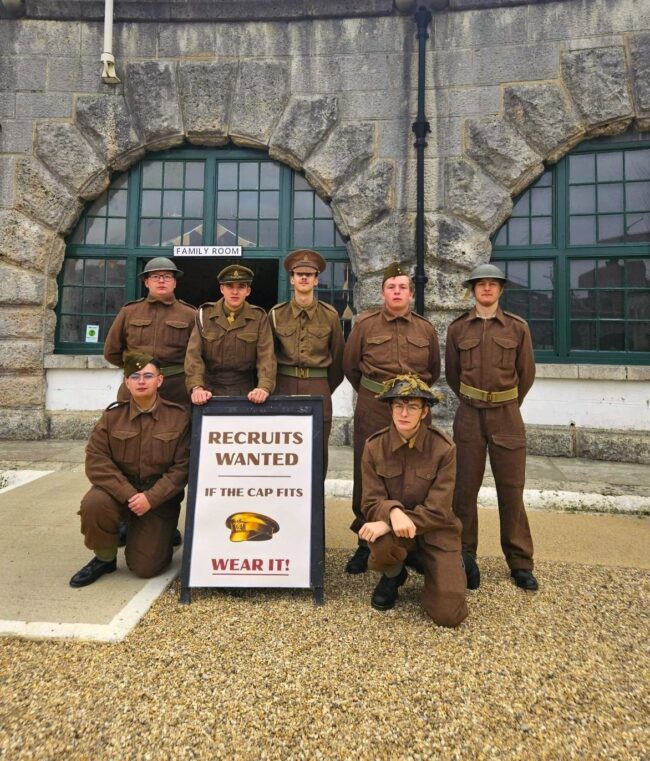 The WW2 Garrison pose in the Parade Ground in front of a wartime recruitment poster.