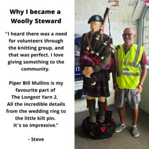 A photo of Steve, a steward in a hi-viz yellow jacket standing beside their favourite knitted figure of Piper Bill Mullins. The text reads: "I heard there was a need for volunteers through the knitting group, and that was perfect. I love giving something to the community. Piper Bill Mullins is my favourite part of The Longest Yarn 2. All the incredible details from the wedding ring to the little kilt pin. It’s so impressive.” - Steve