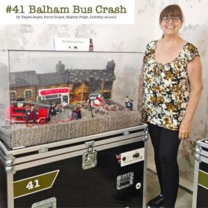 A photo of knitter Tanya Roper standing beside their knitted panel #41 Balham Bus Crash